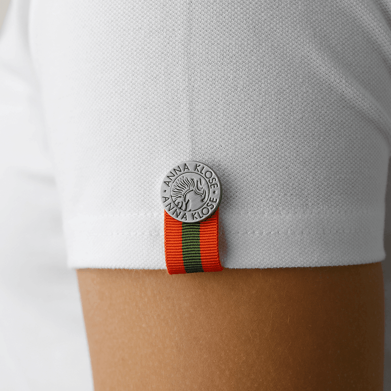 Close-up of the logo button on the sleeve hem of a white polo shirt by Anna Klose Hamburg