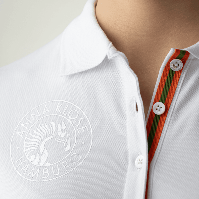 Close up of stylish logo button on sleeve hem of a white polo shirt by Anna Klose Hamburg